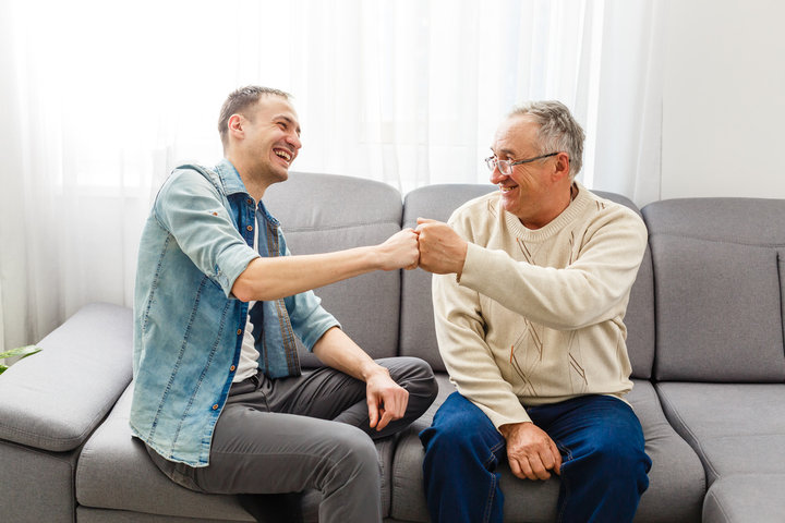 son visiting his older dad in care home and laughing on sofa