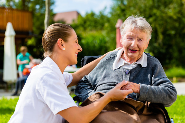 Nurse holding hands with senior woman in wheelchair